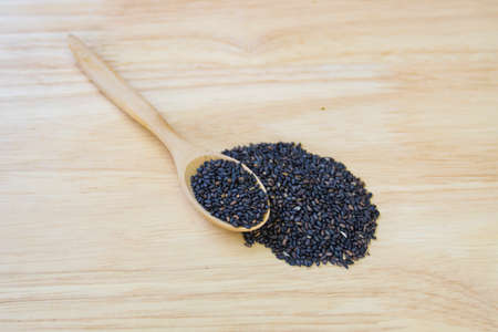 Black sesame seeds in wooden spoon pile on wood tableの写真素材