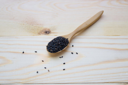 Black sesame seeds in wooden spoon pile on wood tableの写真素材