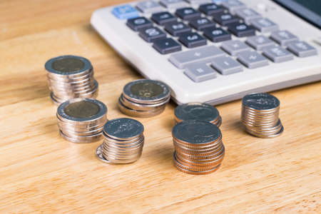stack of coin with blurred calculator for blackground on wood tableの写真素材