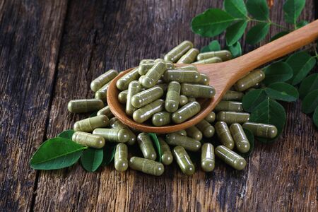 Herbal capsules from moringa leaf on wooden spoonの写真素材