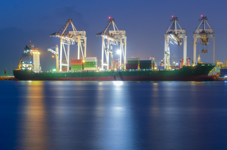 Container Cargo freight ship with working crane bridge in shipyard at dusk for Logistic Import Export at twilightのeditorial素材