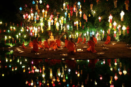 Thai monks meditate around buddha statue among many lanternsのeditorial素材