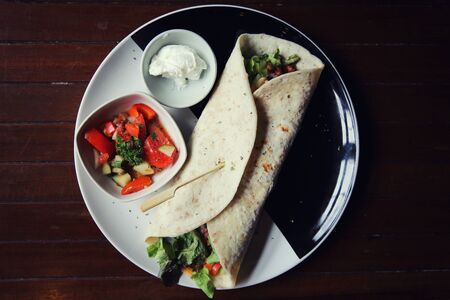 Mexican burritos on a plate with tomato salad