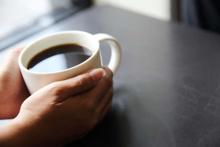 Black coffee with hand on wood background in coffee shopの写真素材