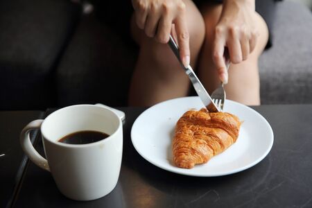 croissant and coffee with girl hand to eating in coffee shopの写真素材