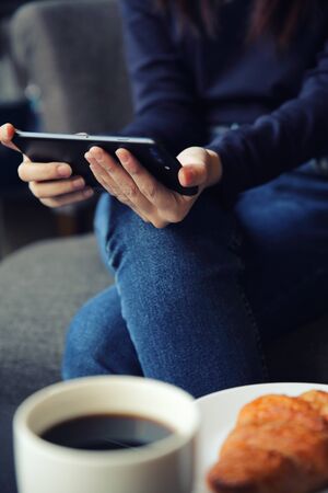 Asian female typing text message with coffe and Croissant