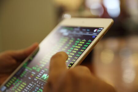 A hand Trading online on tablet with business paper and coffeeの写真素材