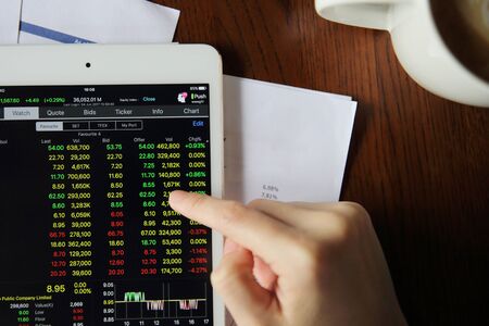 Woman hand Trading online on tablet with business paper and coffeeの写真素材
