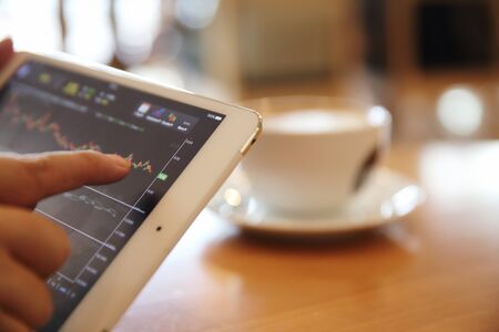 Business Hand Analyzing Stock finance Graph on Tablet with Coffee on wood background
