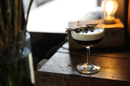 Coffee cocktail with coffee bean and rosemary on top with wood background