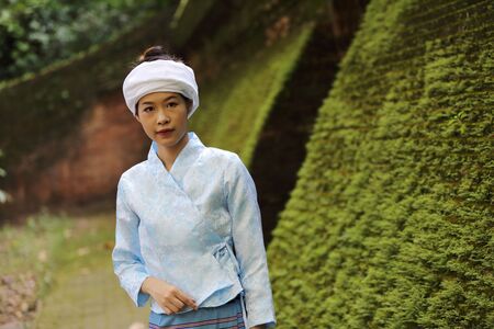 Portrait of thai young woman with traditional thai dress in thai temple with tree and sunrise
