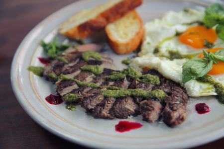 Grilled beef steak with toast , fried egg and vegetables on top with pesto sauce の写真素材
