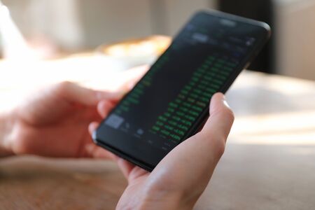 Woman hand trading stock with mobile phone on coffee shop background