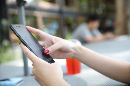 Female hand with smartphone trading stock online in outdoor coffee shop , Business concept