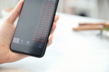 Female hand with smartphone trading stock online in coffee shop , Business conceptの写真素材