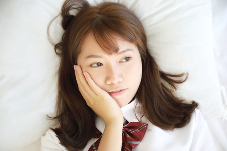 Portrait japanese school girl costume sleeping and smile in white tone bed roomの写真素材
