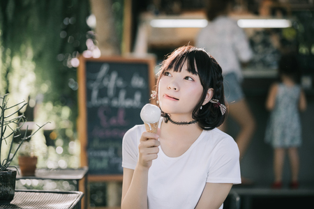 portrait of asian girl with white shirt and skirt eating ice cream in outdoor nature vintage film styleの写真素材