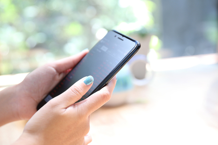 Close up on woman hand holding smartphone trading stock and data in coffee shop background business conceptの写真素材