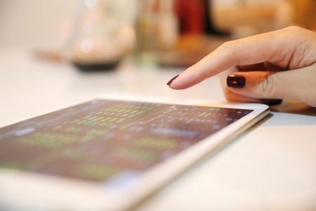 Female hand with tablet trading stock online in coffee shop , Business concept