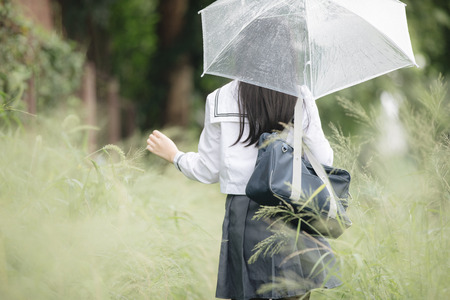 Portrait of Asian school girl walking with umbrella at nature walkway on rainingの写真素材