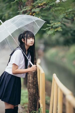 Portrait of Asian school girl walking with umbrella at nature walkway on rainingの写真素材