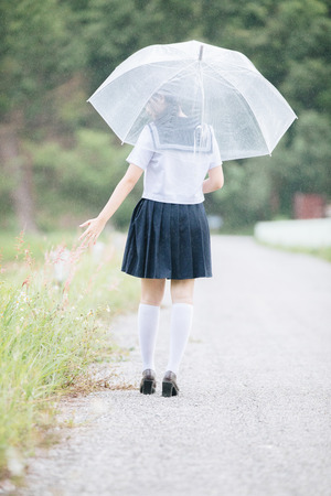 Portrait of Asian school girl walking with umbrella at  nature walkway on rainingの写真素材