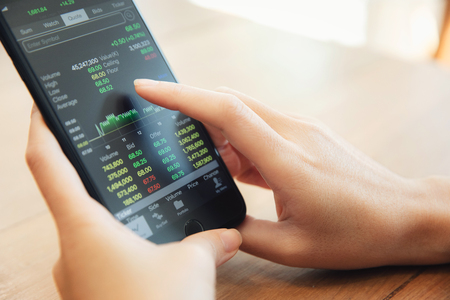 Female hand with smartphone trading stock online in coffee shop , Business conceptの写真素材