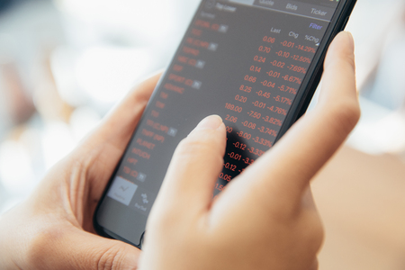 Female hand with smartphone trading stock online in coffee shop , Business conceptの写真素材