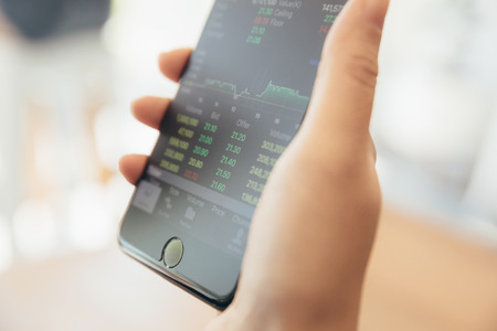 Female hand with smartphone trading stock online in coffee shop , Business conceptの写真素材