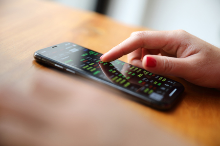 Female hand with smartphone trading stock online in coffee shop , Business conceptの写真素材
