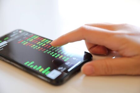 Female hand with smartphone trading stock online in coffee shop , Business concept