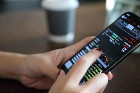 Female hand with smartphone trading stock online in coffee shop, Business concept