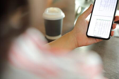 Female hand with smartphone trading stock online in coffee shop , Business concept