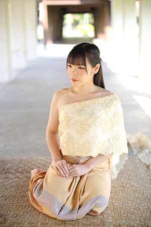 Portrait of Thai female with traditional Thai dress sitting with temple backgroundの写真素材