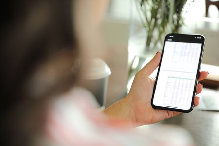 Female hand with smartphone trading stock online in coffee shop , Business conceptの写真素材