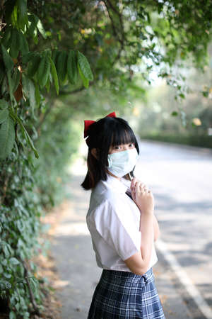 Asian school girl with mask in urban city with tree backgroundの写真素材