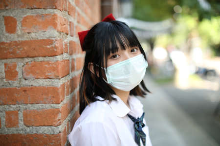 Asian school girl with mask in urban city with tree backgroundの写真素材