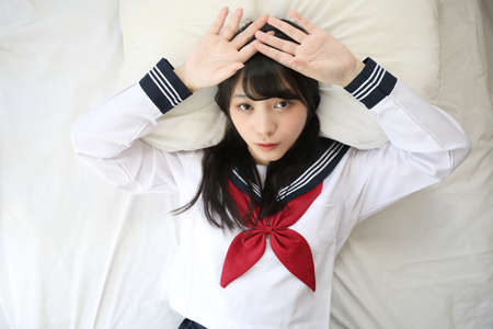 Portrait japanese school girl sleeping with pillow in white tone bed roomの写真素材