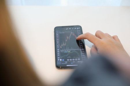 Female hand with smartphone trading stock online in coffee shop , Business conceptの写真素材