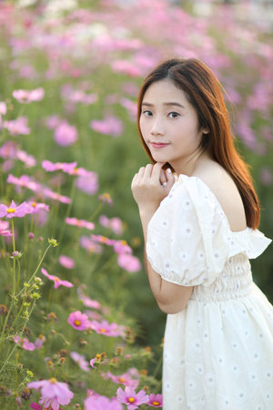 Beautiful young woman with white dress on pink cosmos flowers backgroundの写真素材