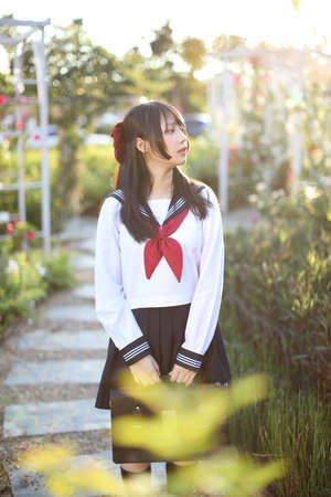 Asian school girl walk and looking with flower garden backgroundの写真素材