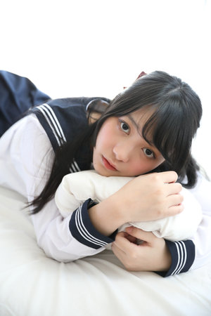 Portrait japanese school girl sleeping with pillow in white tone bed roomの写真素材