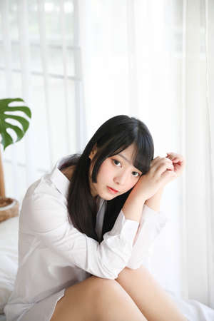Portrait beautiful asian girl sitting with clock at white bedroomの写真素材