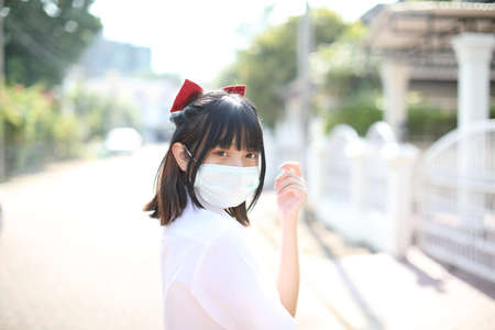 Asian school girl with mask in urban city with tree backgroundの写真素材