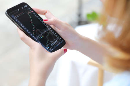 Female hand with smartphone trading stocks online in coffee shop Business conceptの写真素材
