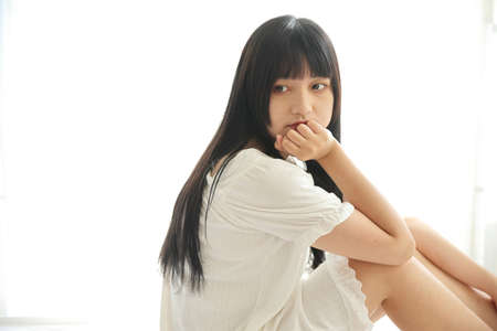 Beautiful young Asian sitting on bed relaxing in the morning light with white room