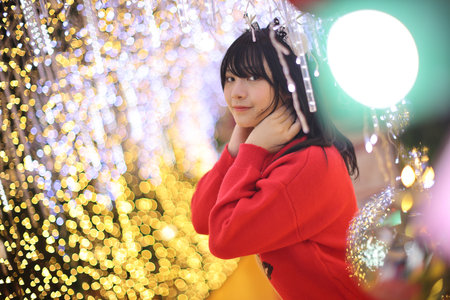 Beautiful Asian young woman with a red sweater with Christmas tree lightの写真素材