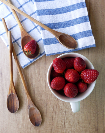 kitchen still life with fresh strawberries in pottery cup, wooden cooking spoons and dishcloths on wooden tableの写真素材