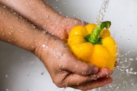 Female hands washing yellow pepperの写真素材