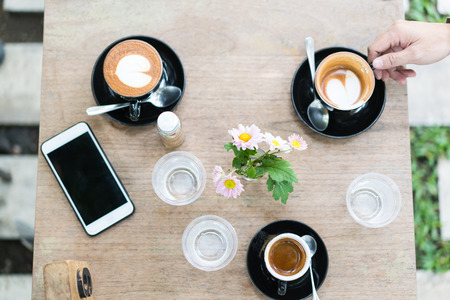 hot coffee in black mug and smart phone on wooden table